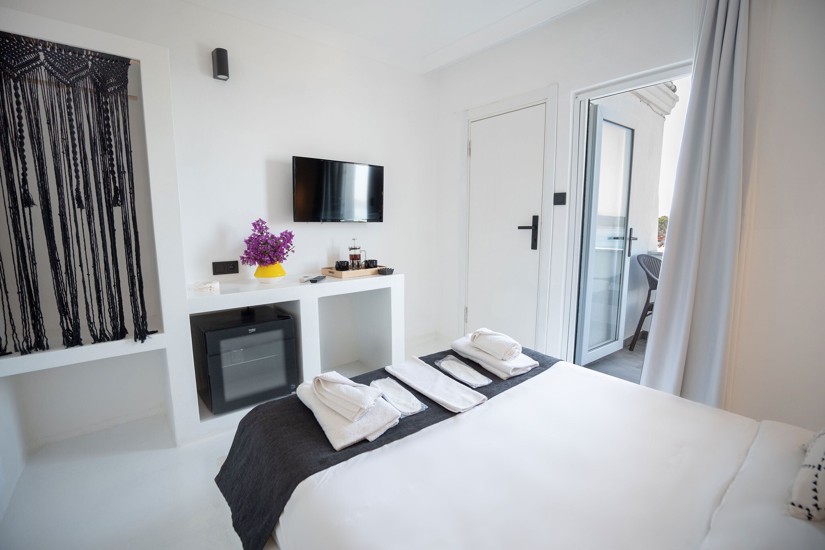 A hotel room with a bed, a flat-screen TV, a minibar, and a view of the outside.