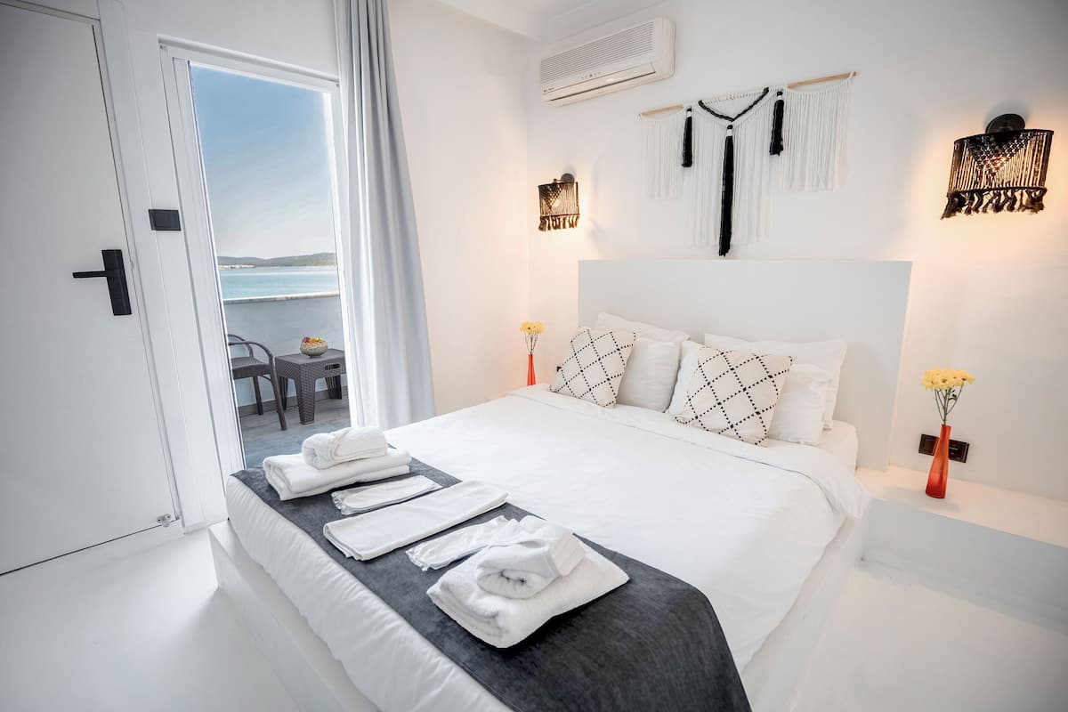 Une chambre d’hôtel moderne avec un lit parfaitement fait, un balcon offrant une belle vue et un décor épuré et minimaliste.