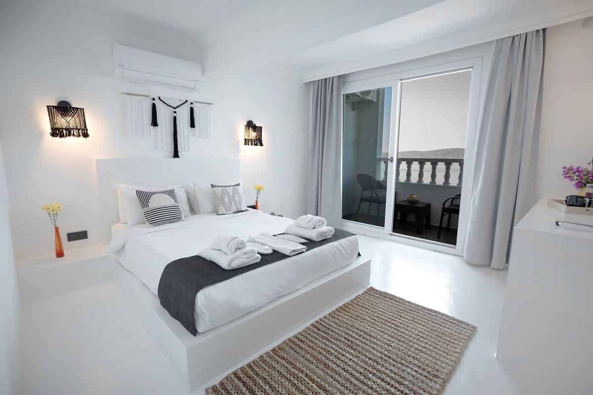 Une chambre moderne avec un grand lit, un balcon offrant une belle vue et une décoration aux tons blancs.