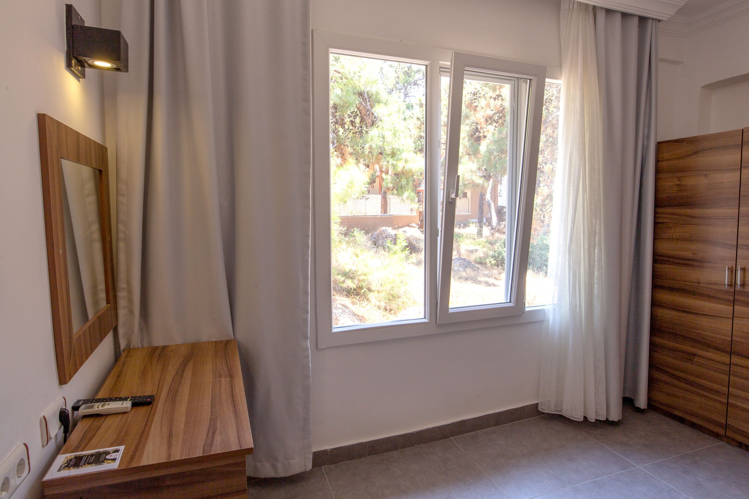 Quarto com escrivaninha de madeira, espelho, janela com cortinas e guarda-roupa.