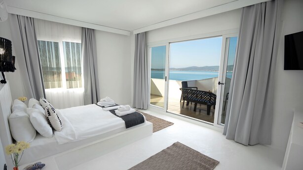 Habitación de hotel moderna con una cama grande, vista al mar y un balcón con mesa y sillas.