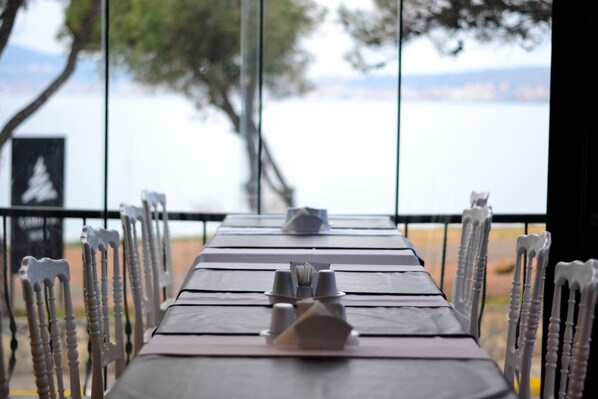 A dining table with chairs, set for a meal, overlooking a body of water. - Camlik 87 Hotel Ayvalik (Ayvalik)