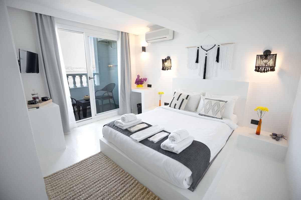 Une chambre moderne avec un grand lit, une télévision et une porte-fenêtre coulissante donnant sur un balcon.