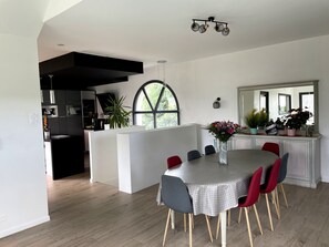 A modern kitchen with a black island, a dining area with a round table and red chairs, and a large window providing natural light. - Villa Kerdelan indoor pool (Baden)