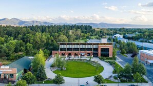 A library with a brick facade, surrounded by a green lawn and trees, with mountains in the background. - *Downtown Luxury + Outdoor Patio*~ Walk Everywhere (Bozeman)