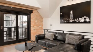 A modern living room with a black leather sofa, a round coffee table, and a hanging light fixture. - *Downtown Luxury + Outdoor Patio*~ Walk Everywhere (Bozeman)