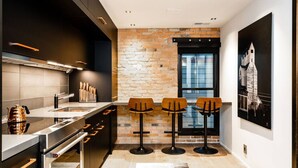 A modern kitchen with a brick accent wall, stainless steel appliances, and two bar stools. - *Downtown Luxury + Outdoor Patio*~ Walk Everywhere (Bozeman)