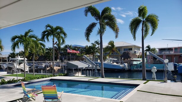 A swimming pool with lounge chairs, palm trees, and boats in the background. - Coo Coo's Nest ~ Key Largo canal front 2/3 with pool (Key Largo)
