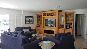 A living room with dark blue sofas, a glass coffee table, and a wooden entertainment unit with a TV. - Coo Coo's Nest ~ Key Largo canal front 2/3 with pool (Key Largo)