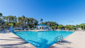 Une piscine rectangulaire, bordée d’une terrasse carrelée, entourée de chaises longues et de palmiers.