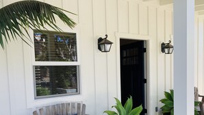 A wooden bench with a cushion, a potted plant, and a black door. - Blue Door Bungalow.  (Montecito)