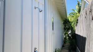 A narrow pathway leading to a white door with a showerhead and a window. - Blue Door Bungalow.  (Montecito)