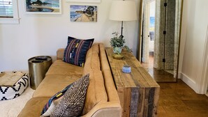 A living room with a brown sofa, a wooden coffee table, and a lamp. There are framed artworks on the wall and a large mirror. - Blue Door Bungalow.  (Montecito)