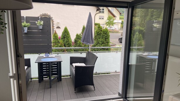 A balcony with a table and chairs, a potted plant, and a view of the street and greenery. - Ferienwohnung mit Balkon (Bruttig-Fankel)