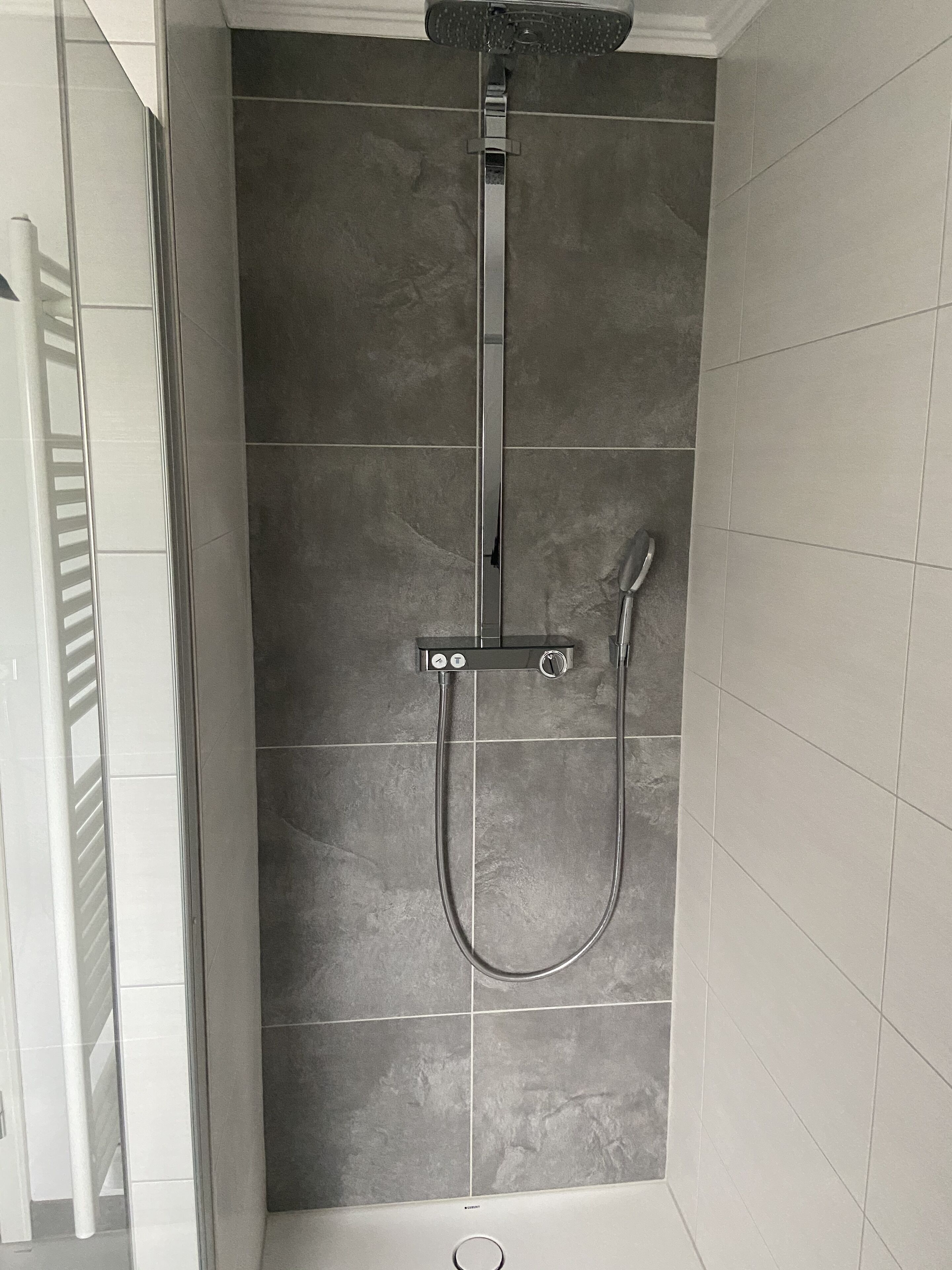 Una ducha con cabezal de ducha de mano y cabezal de ducha fijo en el techo, montada en una pared con azulejos.