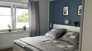 A bedroom with a bed, a window with curtains, a radiator, and a wall with framed pictures. - Ferienwohnung mit Balkon (Bruttig-Fankel)
