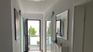 A hallway with a wooden floor, white walls, and a large mirror on the right. There is a door on the left and a window at the end of the hallway. - Ferienwohnung mit Balkon (Bruttig-Fankel)