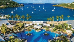 Un resort con piscina centrale, palme e vista sul mare con barche.