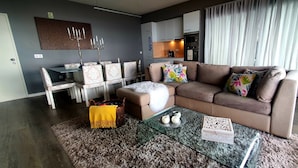 Un salon moderne avec un canapé marron, une table basse en verre et un coin repas comprenant des chaises à motifs et un chandelier.