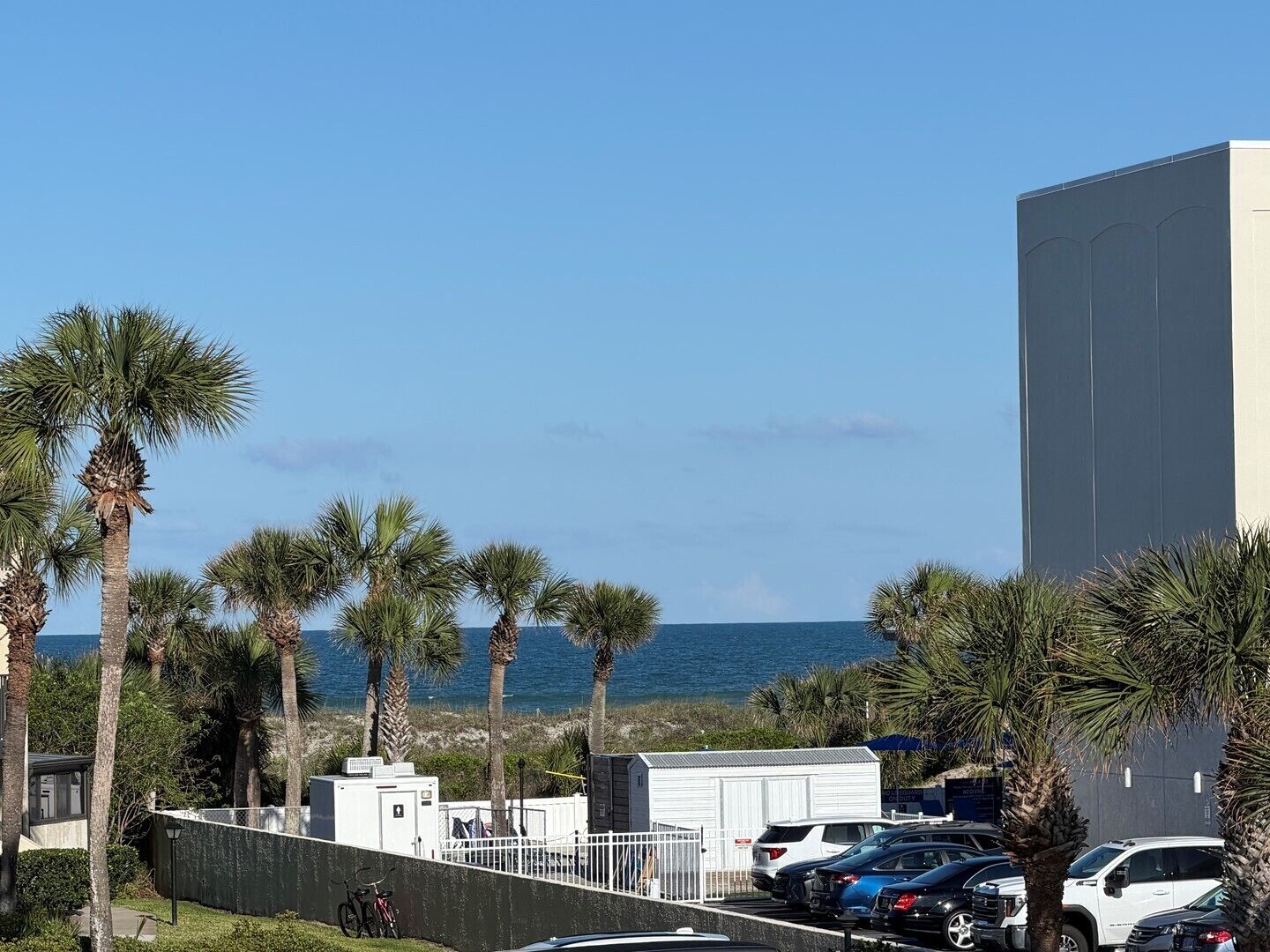 A parking lot with several cars, a white building, and palm trees.
