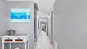 A hallway with a sign saying "Relax You're at the Beach" and a white console table with decorative items. - 2 Bedroom Pet-friendly ocean view condo - OV3 (St Augustine)