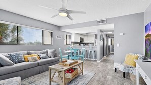 A modern living room with a grey sofa, a wooden coffee table, and a ceiling fan. - 2 Bedroom Pet-friendly ocean view condo - OV3 (St Augustine)