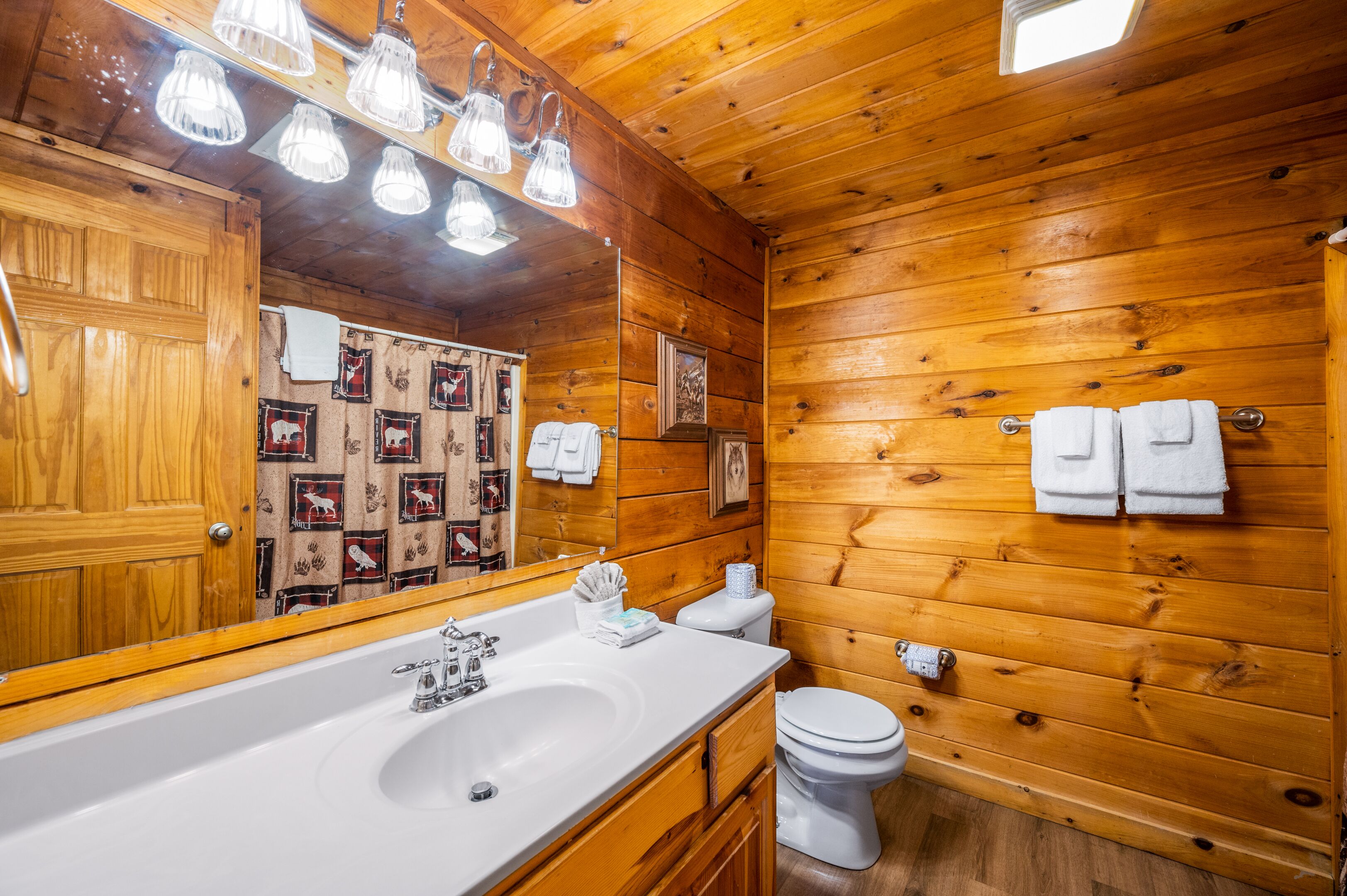 A wooden cabin bathroom with a large mirror, a sink, and a toilet.