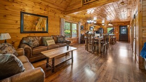 Interior de una cabaña de madera con sala de estar, comedor y cocina.