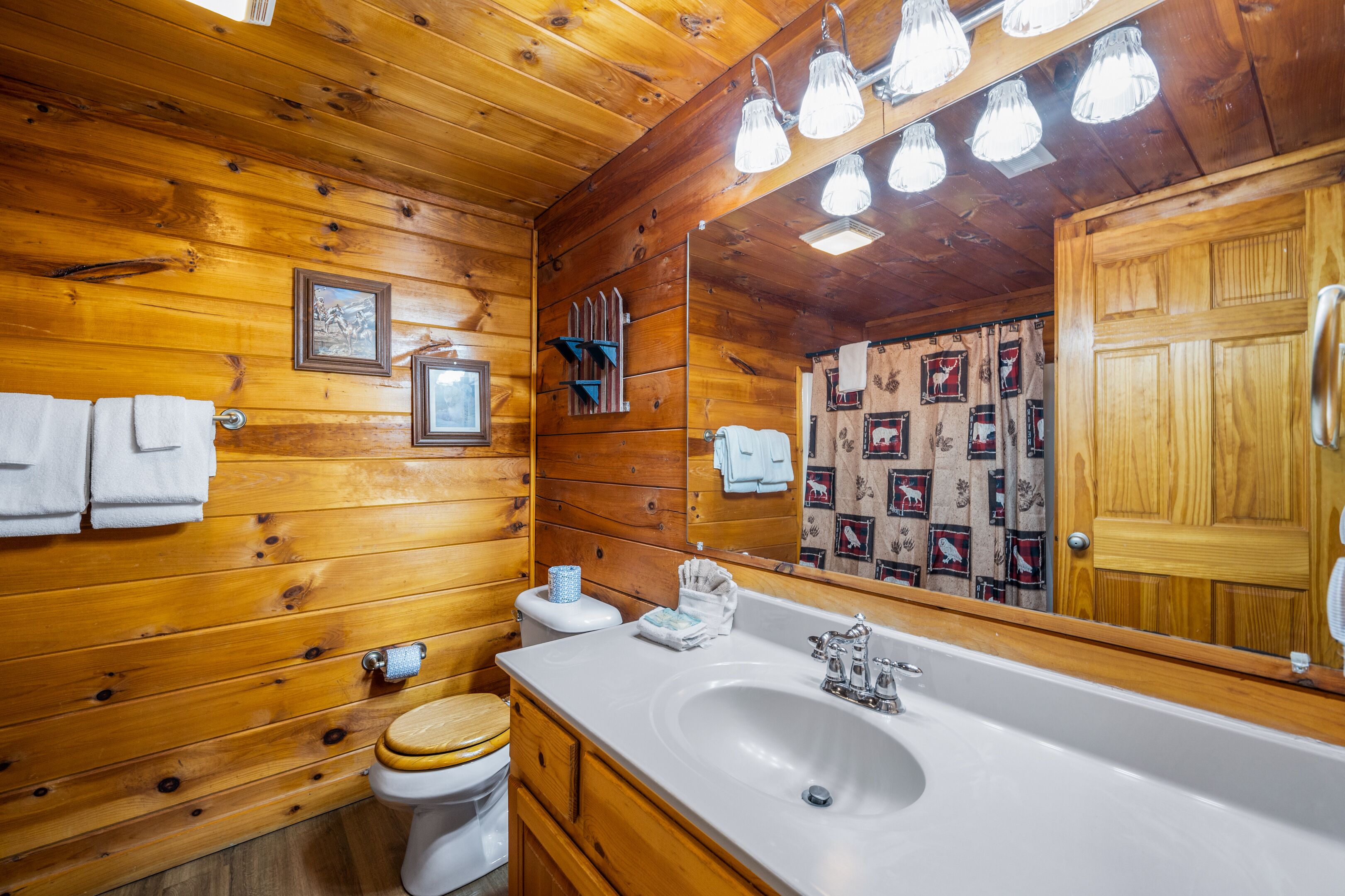 A wooden cabin bathroom with a large mirror, wooden cabinets, a sink, and a toilet.