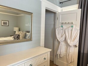 A bedroom with a bed, a dresser, a mirror, and a door with two robes hanging.