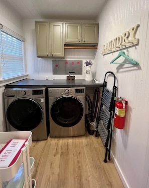 A compact laundry area with two front-loading washing machines, a drying rack, and a fire extinguisher. - Waterfront Historic Bungalow Three• Ferry to SF (Vallejo)