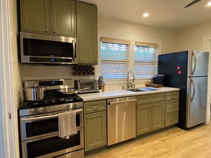 A kitchen with stainless steel appliances, including a stove, oven, microwave, and refrigerator. There is a sink with a faucet, and the cabinets are green.