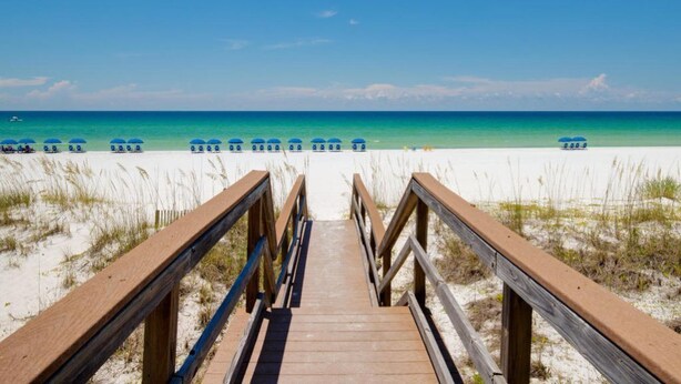 A wooden boardwalk leading to a beach with blue umbrellas and a clear blue sky. - Seasonal Beach Service & Heated Pool + Golf Cart Included!! (Destin)