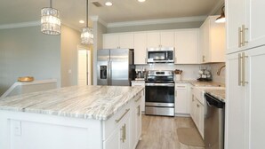 A modern kitchen with white cabinetry, stainless steel appliances, and a marble countertop. - Seasonal Beach Service & Heated Pool + Golf Cart Included!! (Destin)