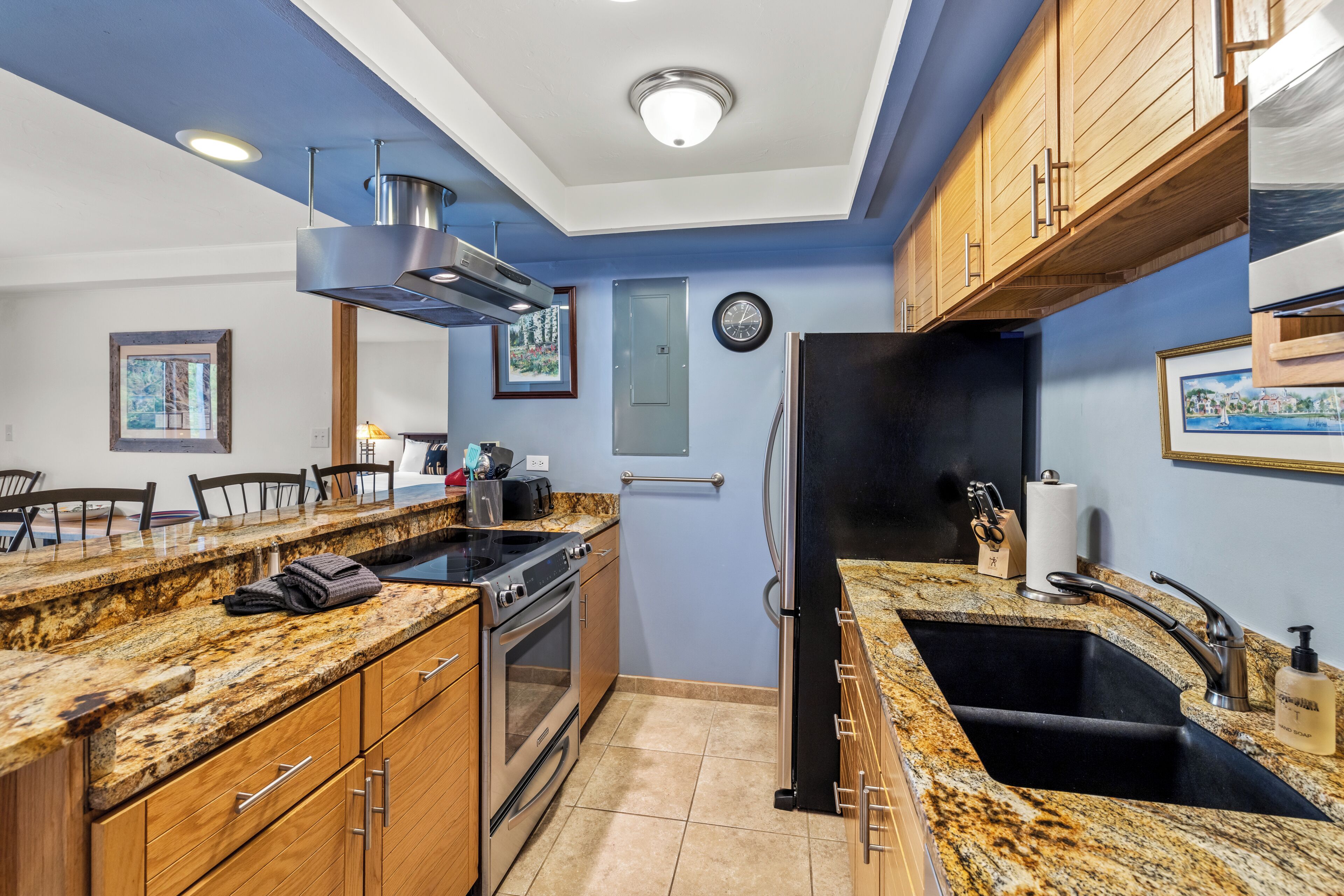 Una cocina con encimeras de granito, electrodomésticos de acero inoxidable, armarios de madera y un refrigerador negro.