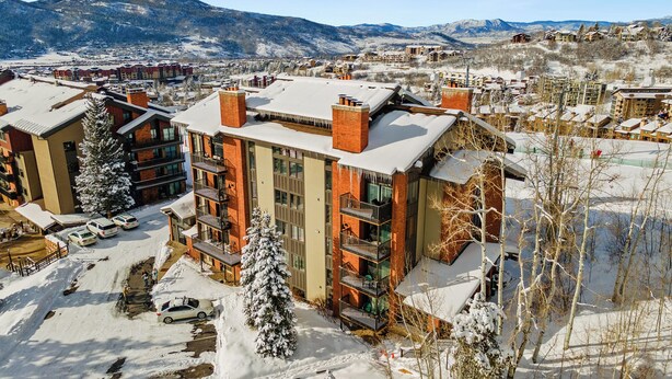 A multi-story hotel with a snow-covered roof, surrounded by a parking area and a mountainous backdrop.
