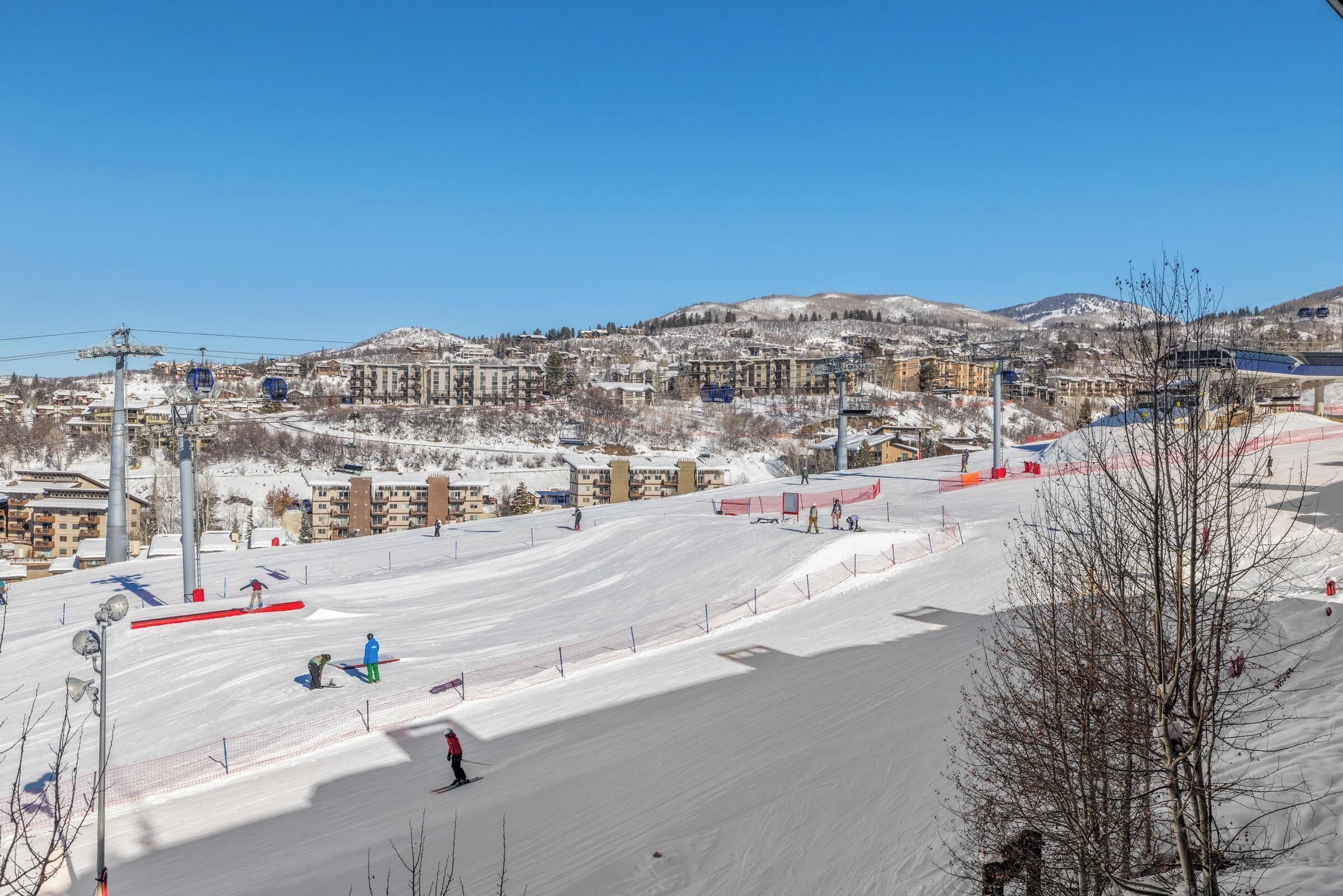 A ski resort with a clear view of the town in the background, ski lifts, and a snow-covered slope.