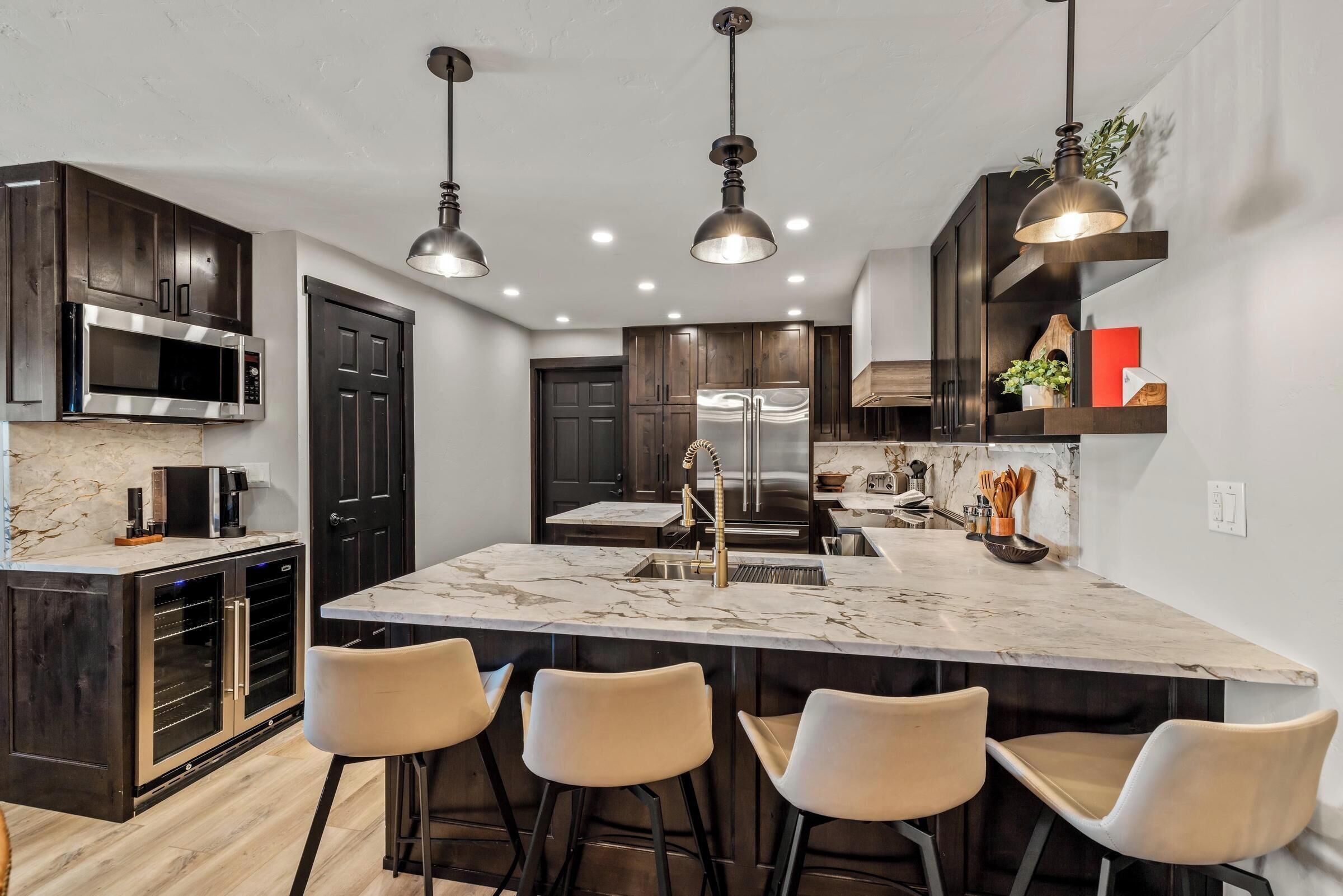 A modern kitchen with dark wood cabinets, stainless steel appliances, and a marble island with bar stools.