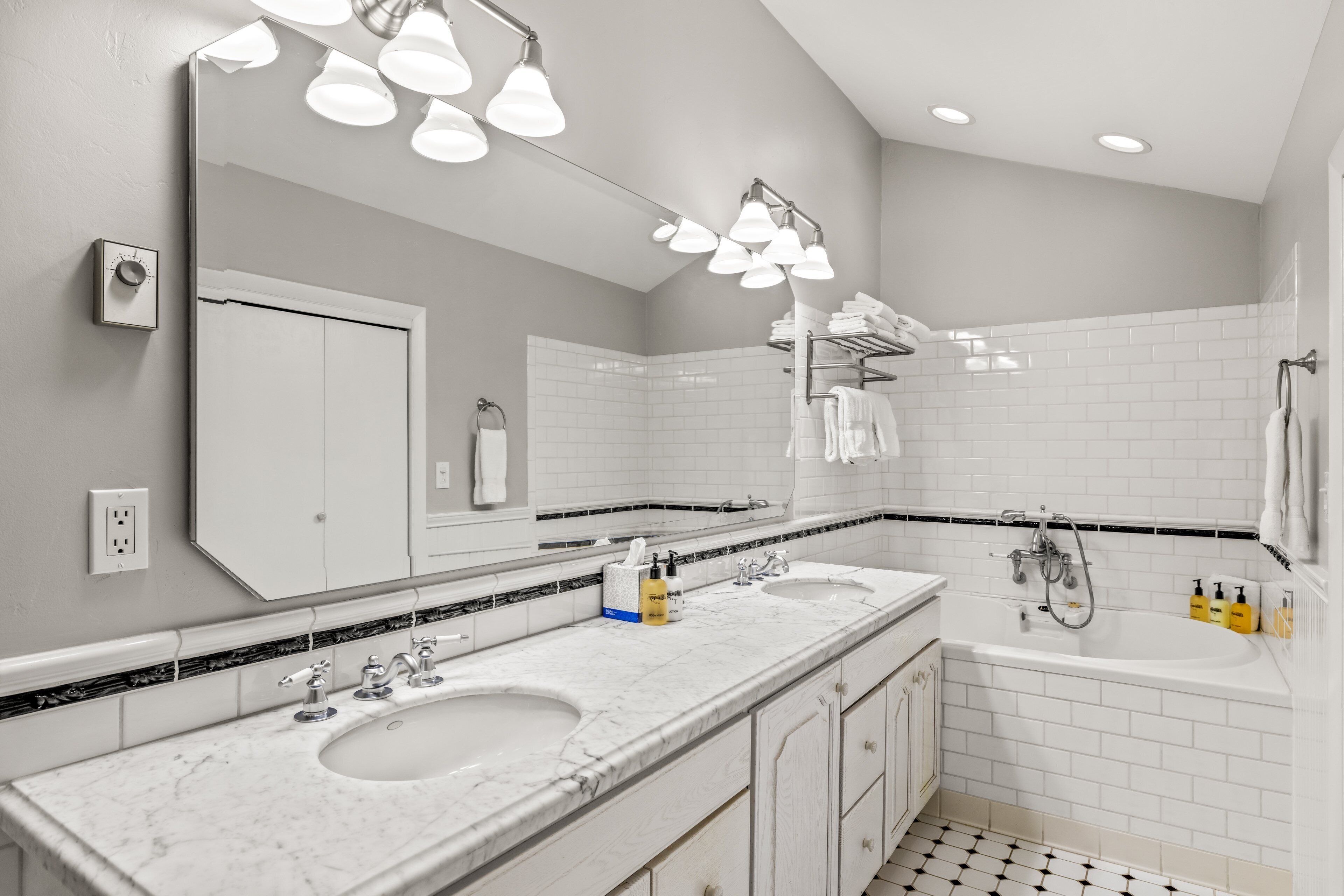 A modern bathroom with two sinks, a large mirror, and a bathtub.