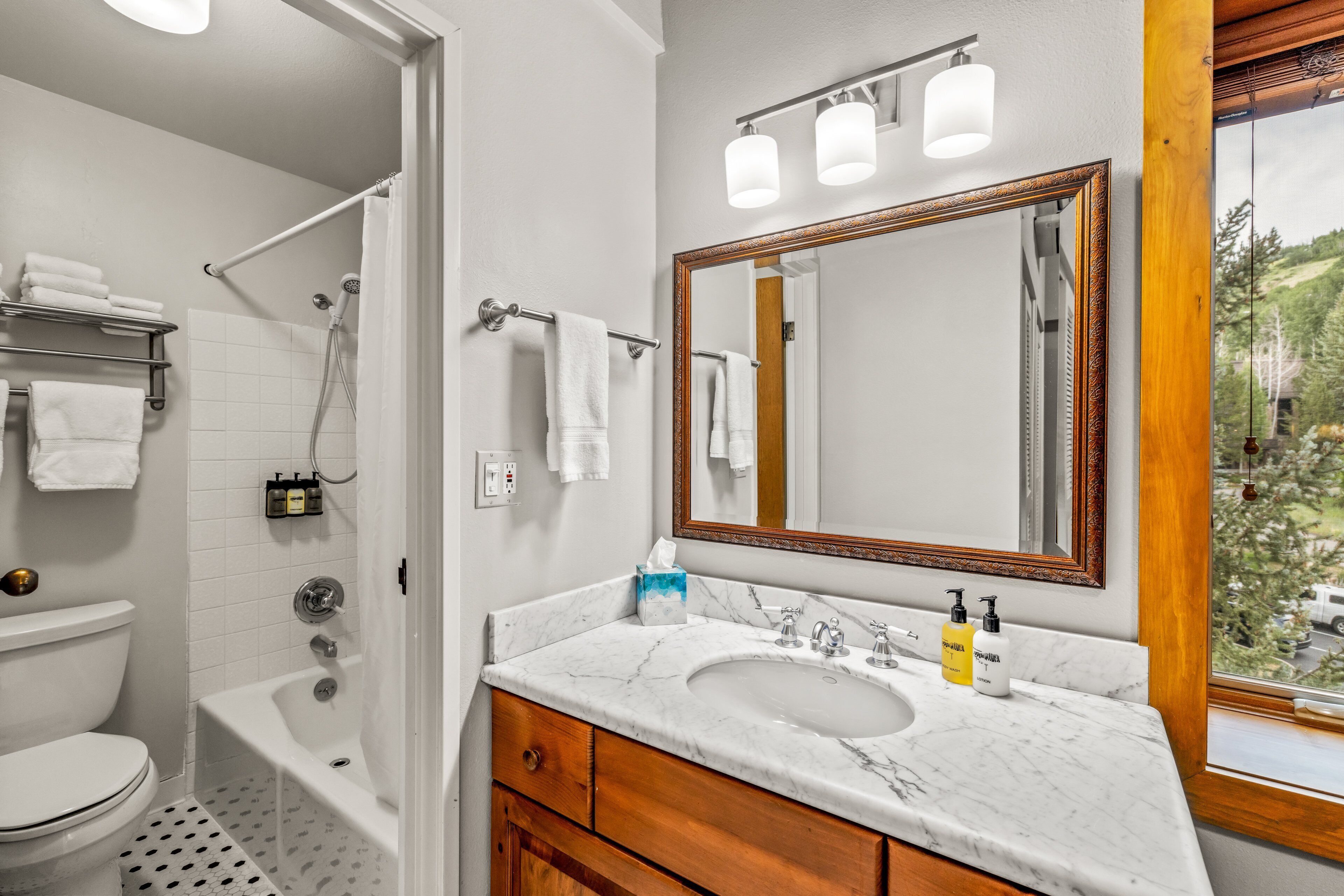 A bathroom with a white toilet, a bathtub, a sink with a marble countertop, and a large mirror.