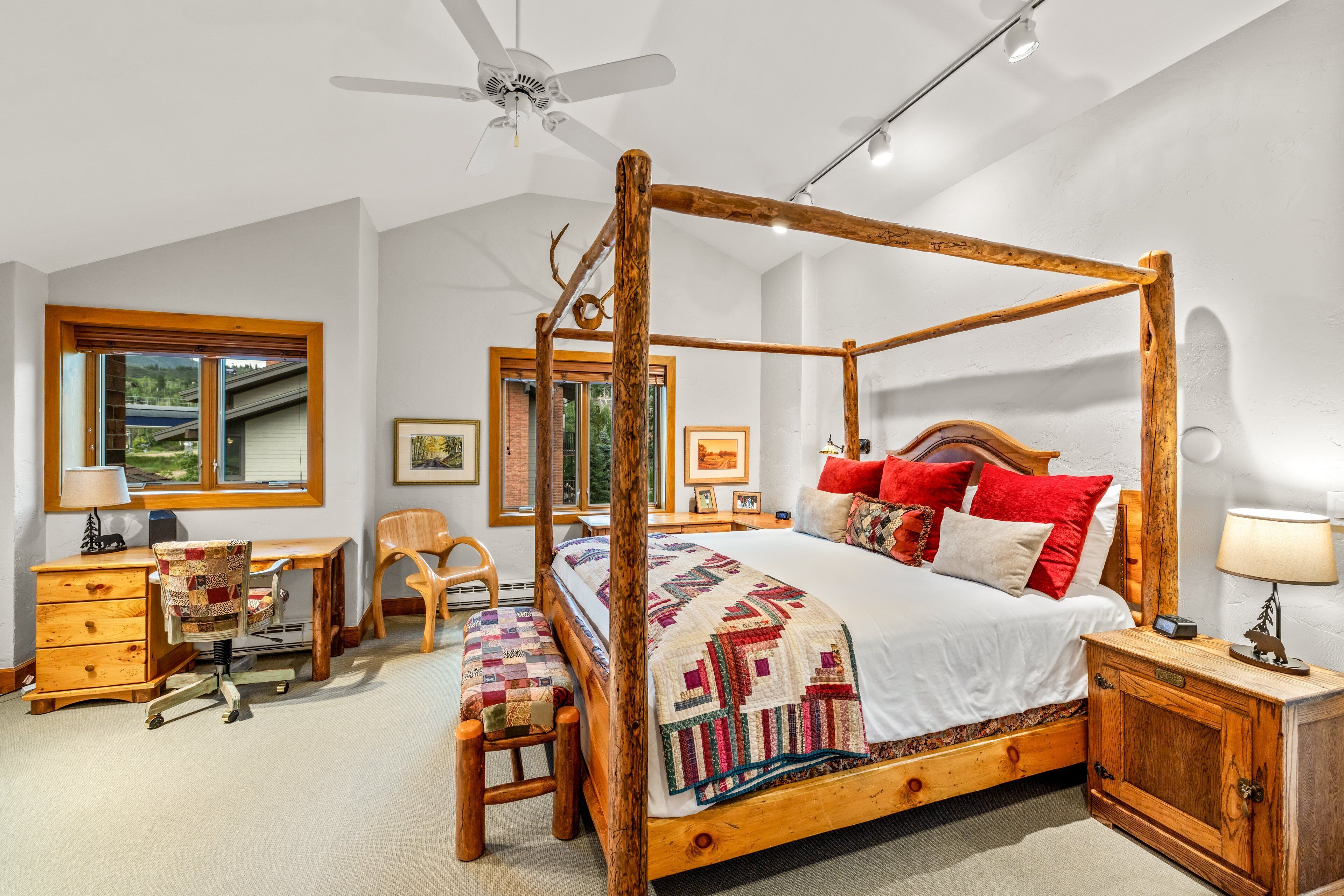 A four-poster bed with a quilt, wooden nightstands, a desk with a chair, and a window with a view.