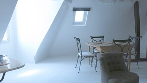 Et værelse med skråvæg, ovenlys, et spisebord med stole og en enkelt lænestol.