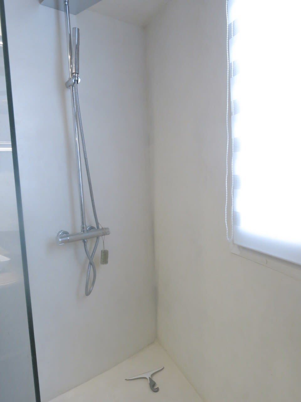A small, white bathroom with a shower, a window, and a towel rack.