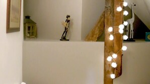 Et soveværelse med skråvæg, en træbjælke, en lille hylde med en figurine og lyskæder.