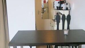 A room with a dark wooden table, a glass of water, and a kitchen area in the background. - Studio Bastille Lappe CityCosy (Paris)