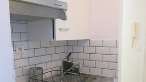 A kitchen with white cabinets, a stainless steel sink, and a black wire basket. - Studio Bastille Lappe CityCosy (Paris)