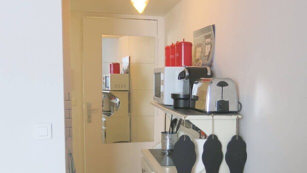 A compact kitchen with white cabinets, a microwave, a coffee maker, and red containers on the counter. - Studio Bastille Lappe CityCosy (Paris)