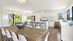 A modern kitchen with white cabinetry, a wooden dining table, and a large window. - Vue Sur La Mer (Wye River)