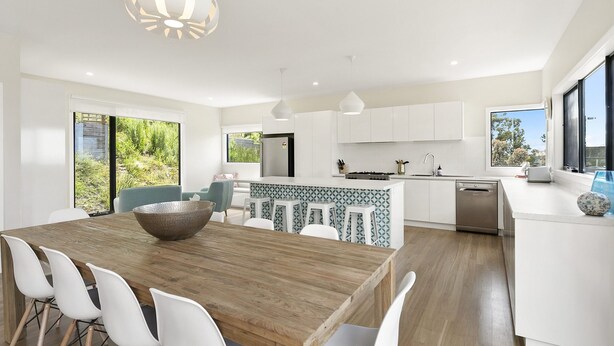 A modern kitchen with white cabinetry, a wooden dining table, and a large window. - Vue Sur La Mer (Wye River)