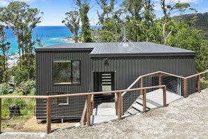 A modern, dark-colored cabin with a metal roof, a wooden staircase, and a metal railing. - Vue Sur La Mer (Wye River)